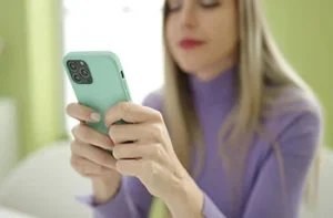 mulher loira de blusa roxa com celular de capa verde fazendo colagens de fotos